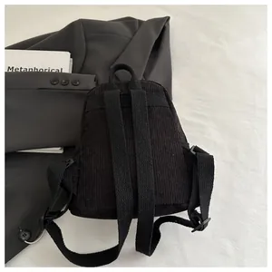 Detailansicht eines schwarzen Cord-Rucksacks auf einem grauen Sakko und weißen Büchern
