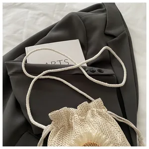 Dettaglio borsa a secchiello in paglia beige con decorazioni floreali e tracolla in corda