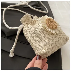 Dettaglio borsa a secchiello in paglia intrecciata con fiore 3D e tracolla bianca