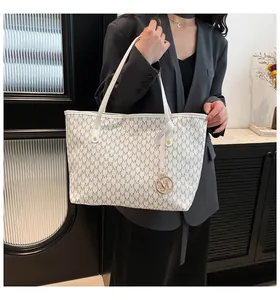 Nahaufnahme der weißen Shopper-Tasche mit M-Muster, Goldanhänger und schmalen Trageriemen