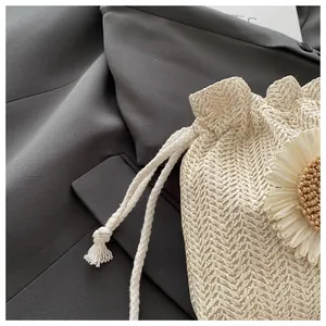 Dettaglio della borsa a secchiello in paglia crema con un grande fiore intrecciato decorativo