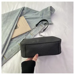 Detail of black crossbody bag with twill texture and chunky silver chain strap on denim