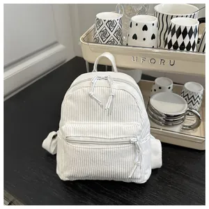 Detailtextur des cremeweißen Cord-Minirucksacks auf einem rustikalen Holztisch