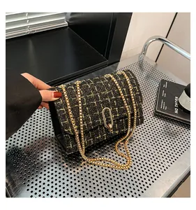 Gros plan du sac bandoulière en tweed noir et doré avec chaîne et fermoir pivotant