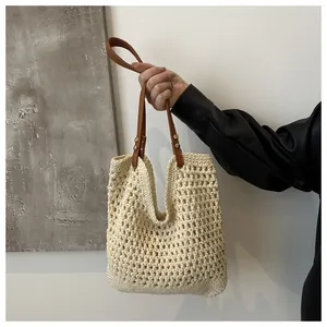 Detail of woven tote bag featuring cream mesh texture and brown leather handles with rivets