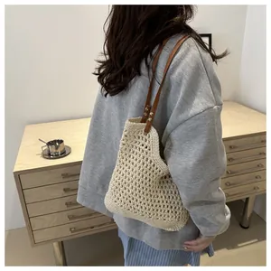 Detail of hollow woven tote bag with brown leather straps shown on model in a cozy setting