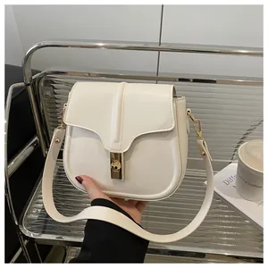 Close-up of beige faux leather saddle bag featuring gold metal twist lock and wide strap
