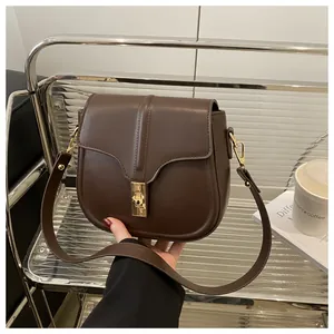 Detailed view of dark brown saddle bag with golden metal twist lock and smooth leather texture