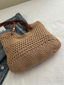Khaki woven hollow tote bag with brown leather straps and metal rivets on denim background