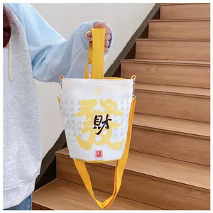 Detail der gelben Canvas-Beuteltasche mit Kalligrafie-Druck und verstellbarem Schultergurt