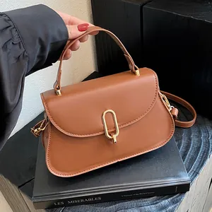 Classic caramel saddle bag with gold oval clasp on black display stand