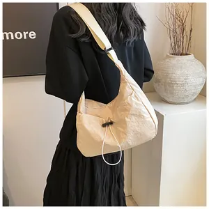 Dettaglio della borsa a mezzaluna beige pieghettata con tracolla larga indossata dal modello