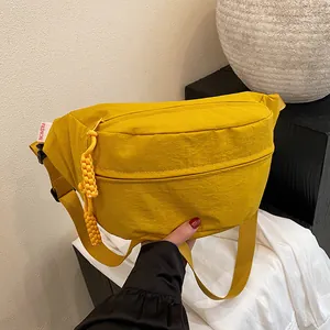 Minimalist yellow nylon crossbody chest bag with wide strap and woven charm detail