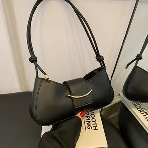 Minimalist black leather shoulder bag with gold metal hardware and knot strap detail