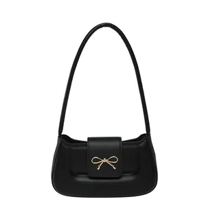 Minimalist black baguette shoulder bag with a gold bow buckle, front view on white background
