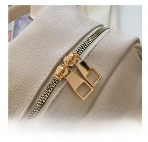 Macro shot of smooth gold-tone dual metal zippers on beige pebbled leather backpack