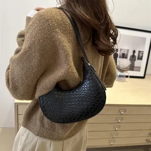 Sac hobo tressé en forme de croissant noir porté à l'épaule dans un décor minimaliste