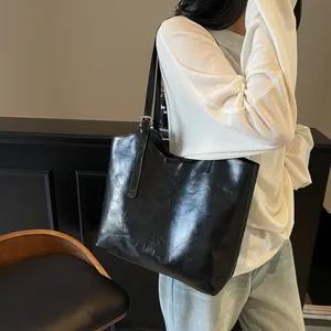 Minimalist large black tote bag in oil-wax leather texture worn on shoulder by model