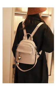 Dettaglio mini zaino beige con texture litchi e ciondolo a bambolina indossato da modella
