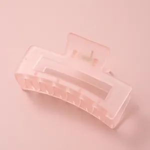 Gros plan sur la pince à cheveux rectangulaire évidée rose pêche mat avec ressort en métal