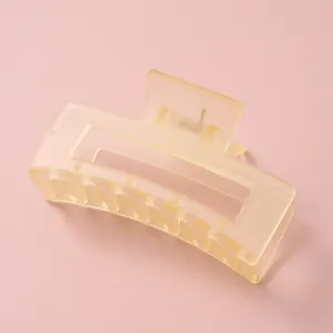 Gros plan d'une pince à cheveux rectangulaire jaune mat sur fond rose doux