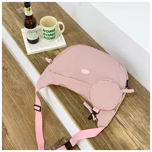 Detail of a pink crescent crossbody bag with a small pouch on a wooden surface