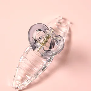 Pinza de pelo transparente de 11cm con mango de corazón y muelle dorado sobre fondo rosa