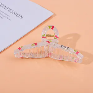 Detail of a large clear resin hair claw clip with cherry patterns and gold spring