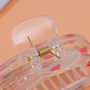 Cute transparent strawberry claw clip with gold spring detail on light orange background