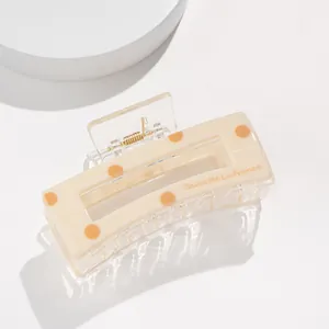 Detail of a beige acrylic hair claw with orange polka dots and La France lettering