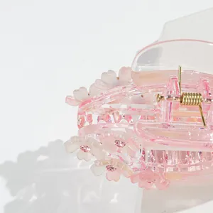 Detailed macro view of pink resin flower hair claw clip with rhinestones on white stand