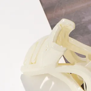 Détail d'une pince à cheveux blanc crème brillante avec un design croisé ajouré élégant