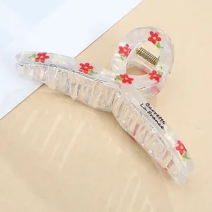 Detail of transparent hair claw clip featuring delicate red floral patterns and metal spring