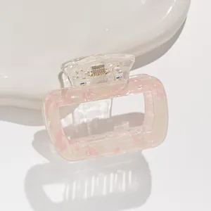 Detail of pink marble hair claw clip with golden spring on a white ceramic tray