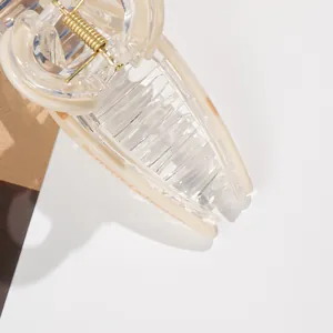 Close-up of a large cream hair claw clip with golden spring and French lettering detail