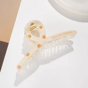 Detailed side view of beige polka dot hair claw clip with golden spring and logo detail