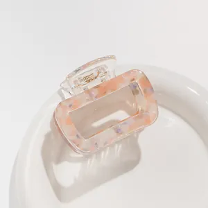 Dettaglio molletta per capelli quadrata in acetato con venature rosa e viola su piatto bianco