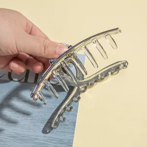 Transparent acrylic hair claw clip with gold foil flakes shown in hand opening pose