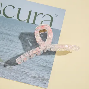 Dettaglio della pinza per capelli in resina rosa con trama marmorea e molla dorata