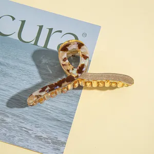 Macro detail of large marble acrylic hair claw clip with golden glitter finish and metal spring