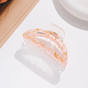 Close-up of translucent pink hair claw clip with golden veins and metal spring detail