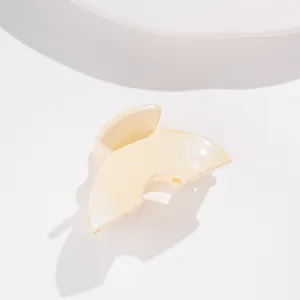 Détail d'une pince à cheveux jaune crème pailletée avec un design en demi-cercle nacré