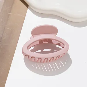 Detail shot of a small oval matte pink hair claw clip on a textured white surface