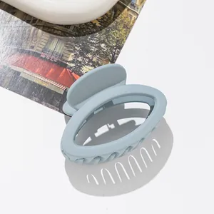 Macro detail of a light blue matte oval hair claw clip with rounded teeth on a white surface