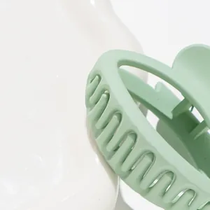 Matte mint green oval hair claw clip for women on a white textured tray