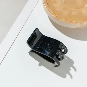 Détail d'une petite pince à cheveux noire avec paillettes bleues sur fond blanc