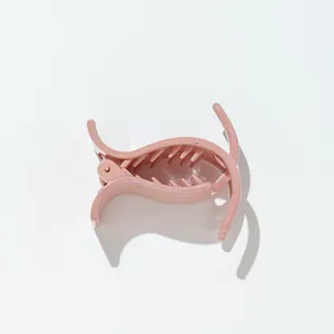 Close-up of a small glitter shark hair clip in soft peach pink with a metal spring