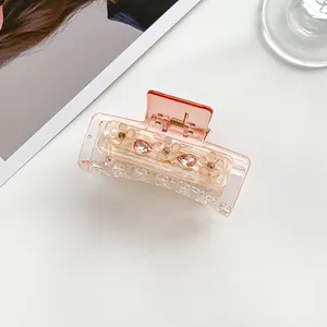 Close-up of translucent peach floral hair claw clip with rhinestones on white surface