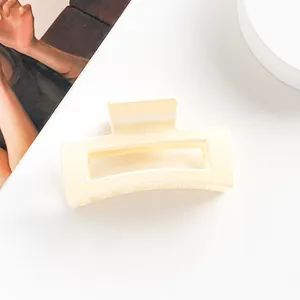 Détail d'une pince à cheveux rectangulaire beige évidée sur fond blanc épuré et moderne