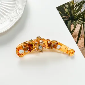 Détail d'une pince banane en résine ambre avec fleurs en cristal et strass brillants